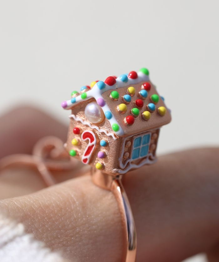 Spinning Gingerbread House Ring in rose gold, close-up worn on a hand, showing the candy roof and front door